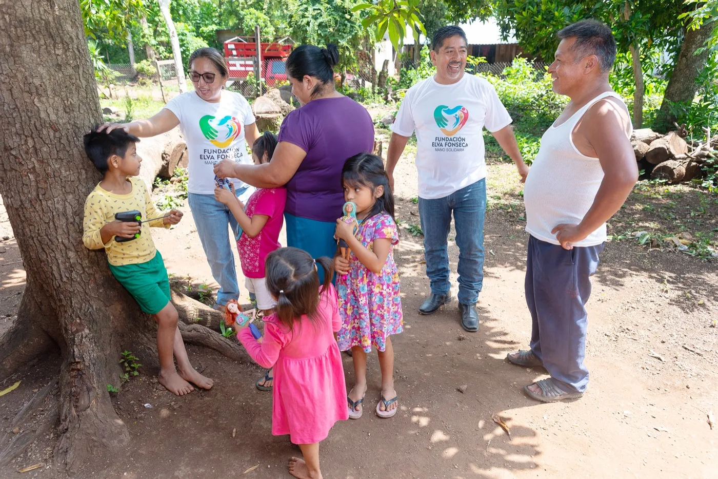 Volunteers and children gathered together outdoors under a tree